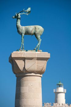 Rhodian deer statue with St Nicholas lighthouse behind. Build on the site of the legendary Colossus of Rhodes the statues guard the harbour to Mandraki Harbour on the greek island of Rhodes.