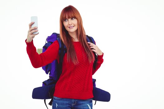 Smiling hipster woman with a travel bag taking selfie against white background