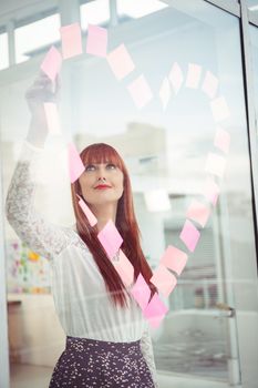 Smiling hipster woman doing a heart in post-it in office