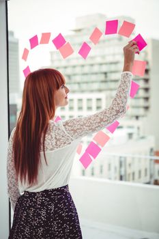 Rear view of a hipster woman doing a heart in post-it in office