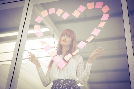 Smiling hipster woman doing a heart in post-it in office