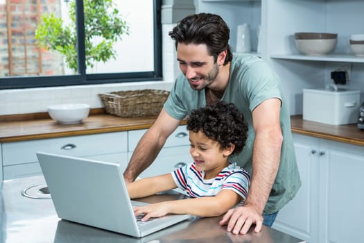 Smiling father using laptop with his son in the kitchen at home