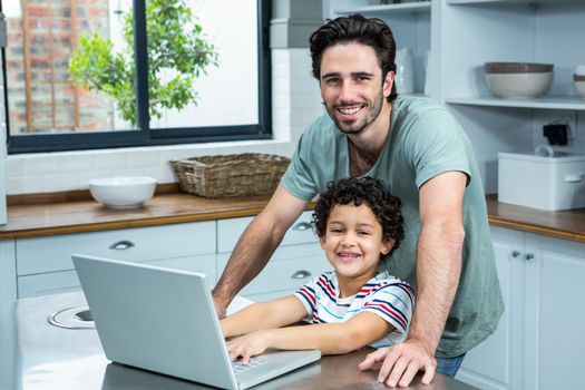 Portrait of smiling father using laptop with his son in the kitchen at home