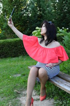 Brunette girl sitting on a park bench and looking at the tablet