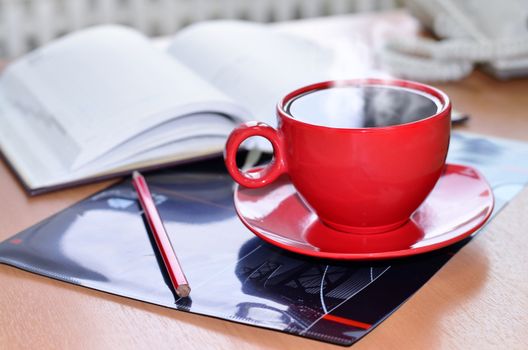 Red cup of hot coffee, notepad and pencil on the desktop in the office