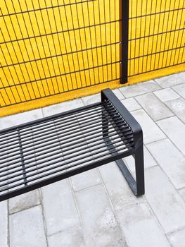 Metal bench near bright yellow playground. Urban architecture.