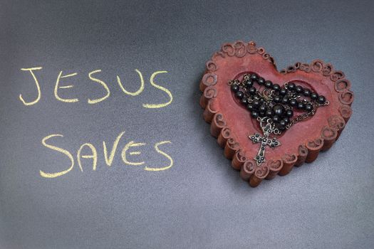 In the picture a rosary iron placed over a heart of red wax, on the left side the inscription "Jesus Saves" made with a crayon.