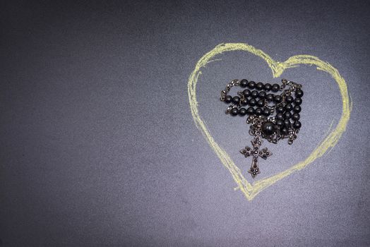 in the picture a rosary iron at the center of a heart drawn with a crayon and copy space in the left side.