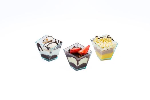 Three cupcakes with chocolate,white chocolate, fruits,cream and custard in a plastic cup,isolated on white background.