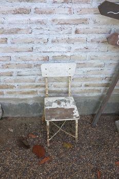 Old white wooden chair leans on white brick wall