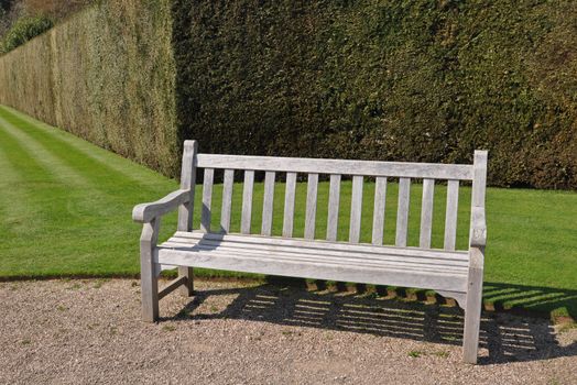 Garden bench, made of wood, within an English country garden with large pristine hedge behind.