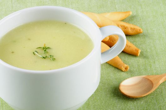 Delicious Cream Asparagus Soup in White Soup Cup with Bread Sticks and Wooden Spoon Cross Section on Green Napkin