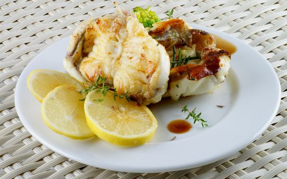 Delicious Roasted White Cod Fish with Herbs, Lemon and Sauce on White Plate closeup on Wicker background