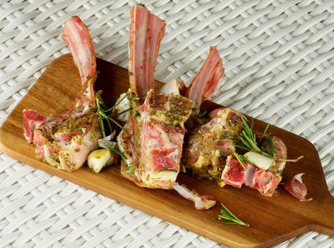 Raw Lamb Ribs in Marinade of Herbs with Rosemary and Garlic closeup on Wooden Cutting Board on Wicker background. Top View