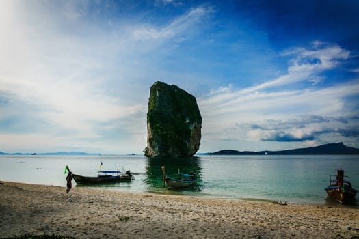 Boat on the beach of Thailand near with a huge rock. Picturesque clear blue sky.