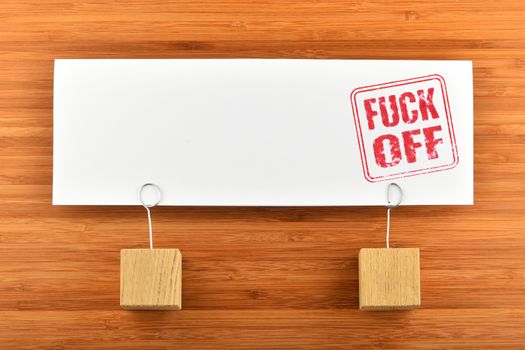 Fuck off red rude stamp on one big white paper note with two wooden holders on wooden bamboo background for presentation