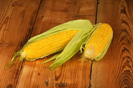 Two open fresh yellow corn cob with green husk on brown vintage wooden surface