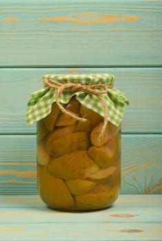 One glass jar of homemade pear compote with green checkered textile top decoration at blue painted vintage wooden surface