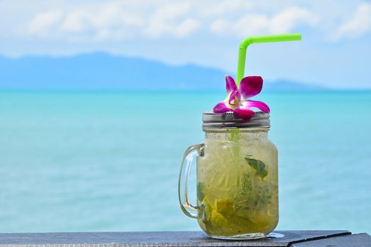 Big jars mug style full glass of fresh frozen mojito with metal cap lid, straw and purple orchid flower in cafe on the beach