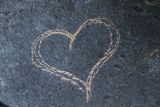Love heart drawn with chalk on a black rock at the coast