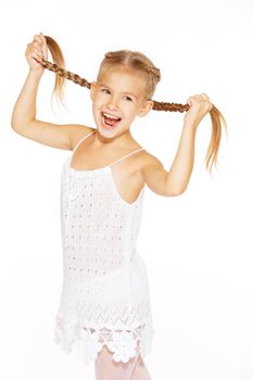 Funny little girl with a charming smile in a white dress holding a pigtails