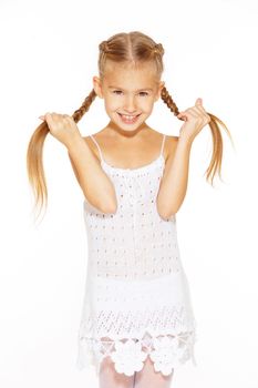 Funny little girl with a charming smile in a white dress holding a pigtails