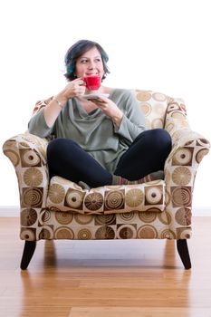 Pleased middle-aged woman at home sitting comfortably in sofa chair enjoying her morning coffee