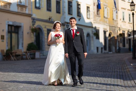 Bride and groom. Portrait of a loving wedding couple, holding hands, walking down cobbled street in medieval city center of Ljubljana, Slovenia.