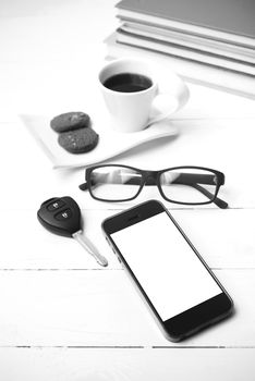 coffe cup with cookie,phone,car key,eyeglasses and stack of book on white wood table black and white color