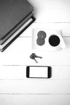 coffee cup with cookie,phone,stack of book and key on white wood table black and white color