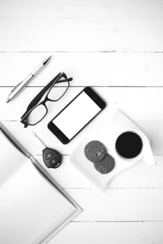 coffee cup with cookie,phone,open notebook,car key and eyeglasses on white wood table black and white color