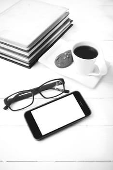 coffee cup with cookie,phone,stack of book and eyeglasses on white wood table black and white color