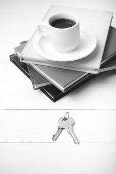 coffee cup,key and stack of book on white wood table black and white color