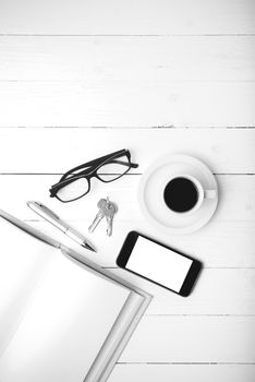 coffee cup with phone, key,eyeglasses and open notebook on white wood table black and white color