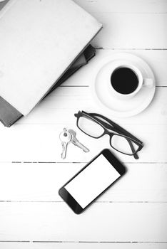 coffee cup with phone,key,eyeglasses and stack of book on white wood table black and white color