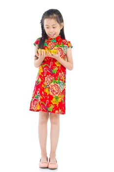 Full length China girl in traditional Chinese cheongsam dress greeting, holding a gold ingot standing isolated on white background