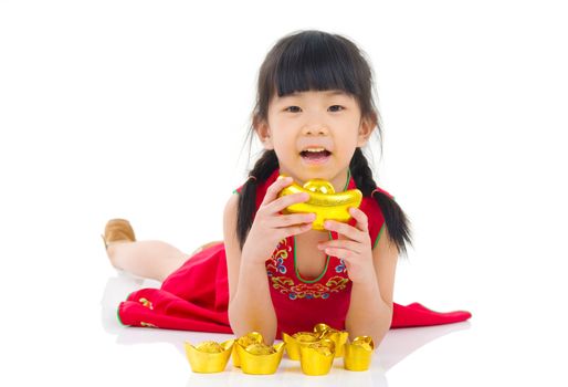 China girl in traditional Chinese cheongsam dress greeting, holding a gold ingot lying down in the studio