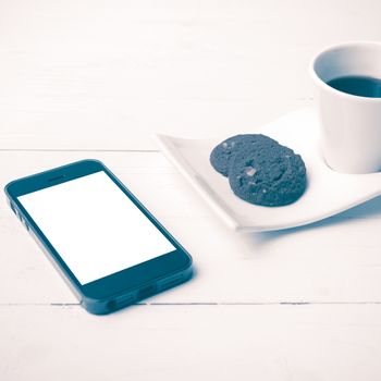 coffee cup with cookie and phone on white wood background vintage style