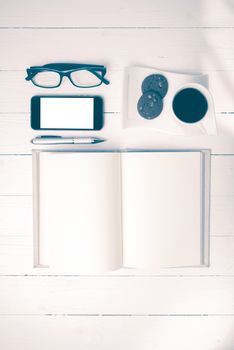 coffee cup with cookie,phone,notebook and eyeglasses on white wood table vintage style