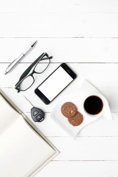 coffee cup with cookie,phone,open notebook,car key and eyeglasses on white wood table