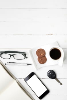 coffee cup with cookie,phone,open notebook,car key and eyeglasses on white wood table