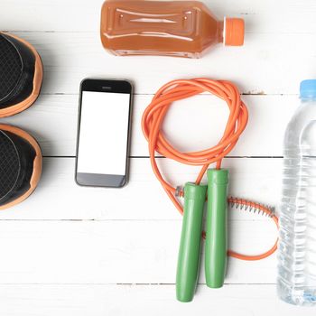 fitness equipment : running shoes,jumping rope,water,juice and phone on white wood background
