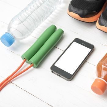 fitness equipment : running shoes,jumping rope,water,juice and phone on white wood background