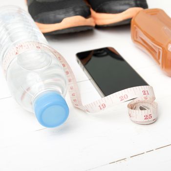 fitness equipment:running shoes,measuring tape,water,juice and phone on white wood background