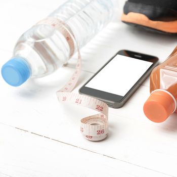 fitness equipment:running shoes,measuring tape,water,juice and phone on white wood background