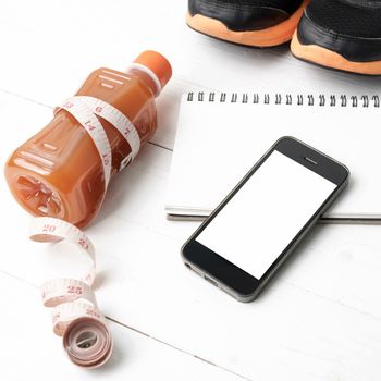 fitness equipment:running shoes,juice,measuring tape,notepad and phone on white wood background