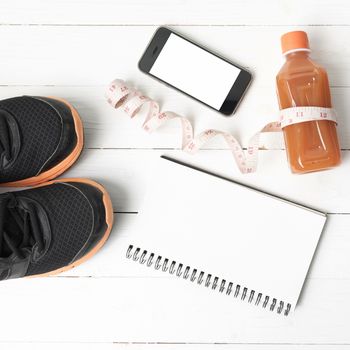 fitness equipment:running shoes,juice,measuring tape,notepad and phone on white wood background