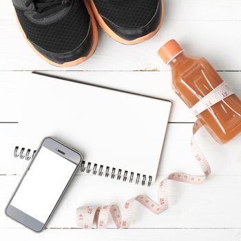 fitness equipment:running shoes,juice,measuring tape,notepad and phone on white wood background