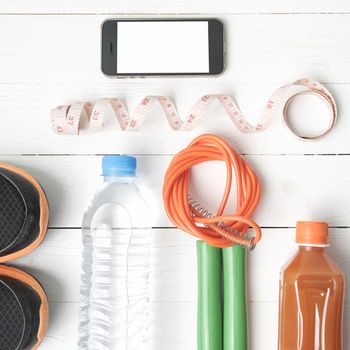 fitness equipment:running shoes,phone,measuring tape,water,juice and jumpong rope on white wood background