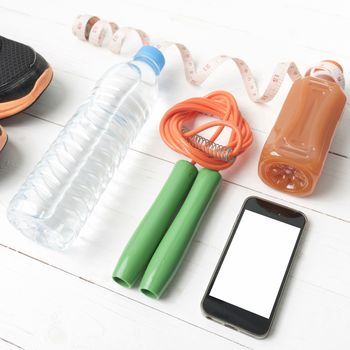 fitness equipment:running shoes,phone,measuring tape,water,juice and jumpong rope on white wood background